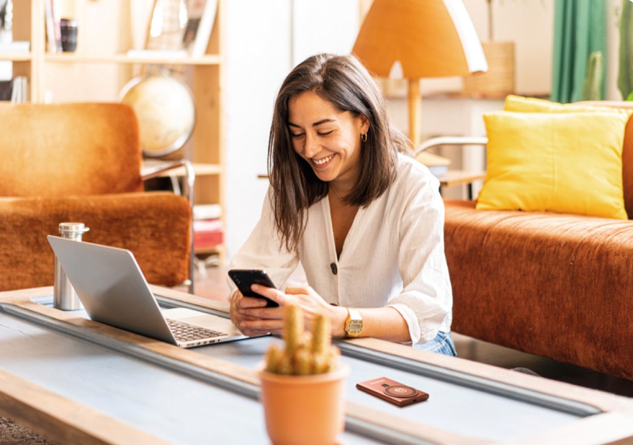 Smiling woman working from home with laptop and smartphone in a remote work setting with personalized gifts
